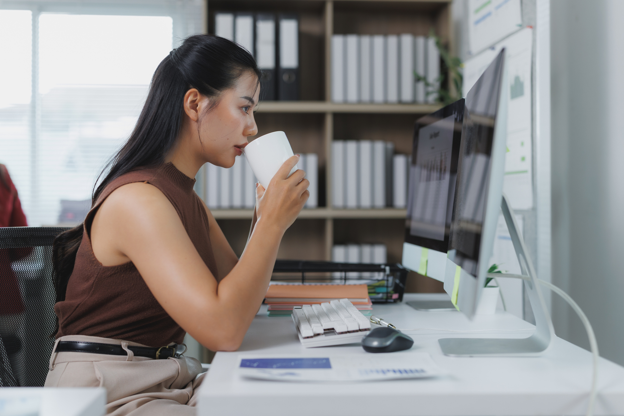 Young businesswoman drinking coffee while working on desktop computer in office