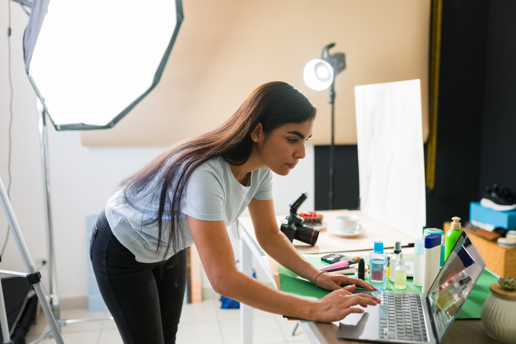 Young woman photographer editing products images using a laptop in a professional photographic studio